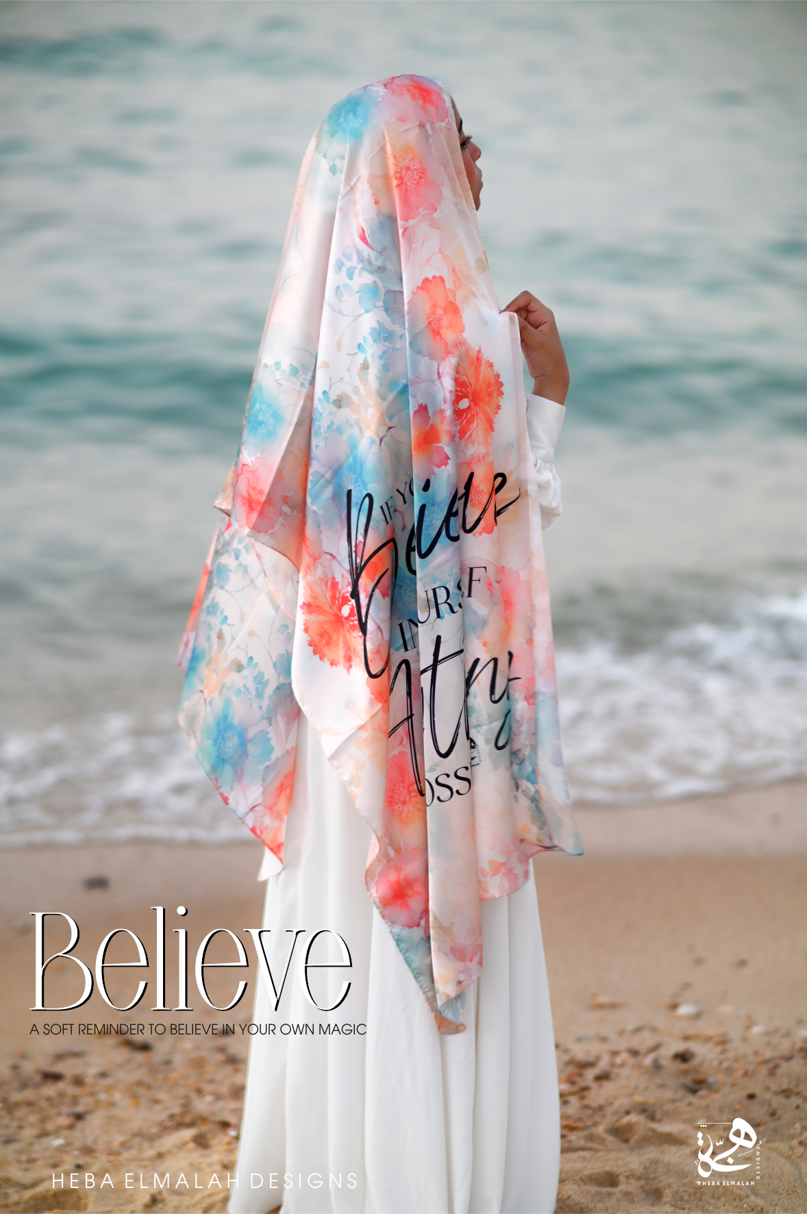Woman wearing the Believe Silk Satin Hijab by Heba Elmalah Designs on the beach, featuring soft coral, aqua, and blush floral prints over a light background.